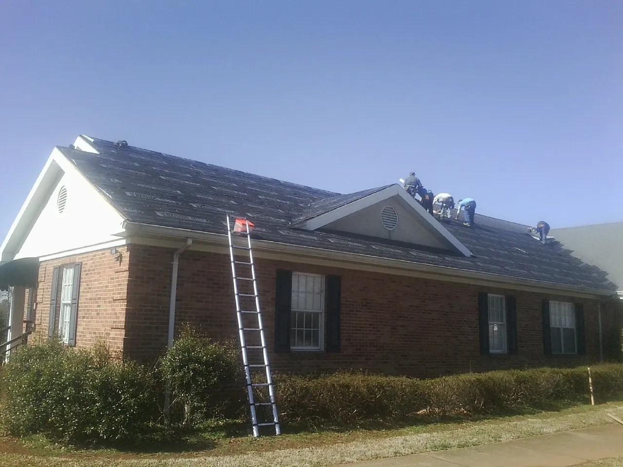 Crew tearing shingles off a brick ranch roof with a ladder set — Emergency Roof Repair work by our crew in Montpelier