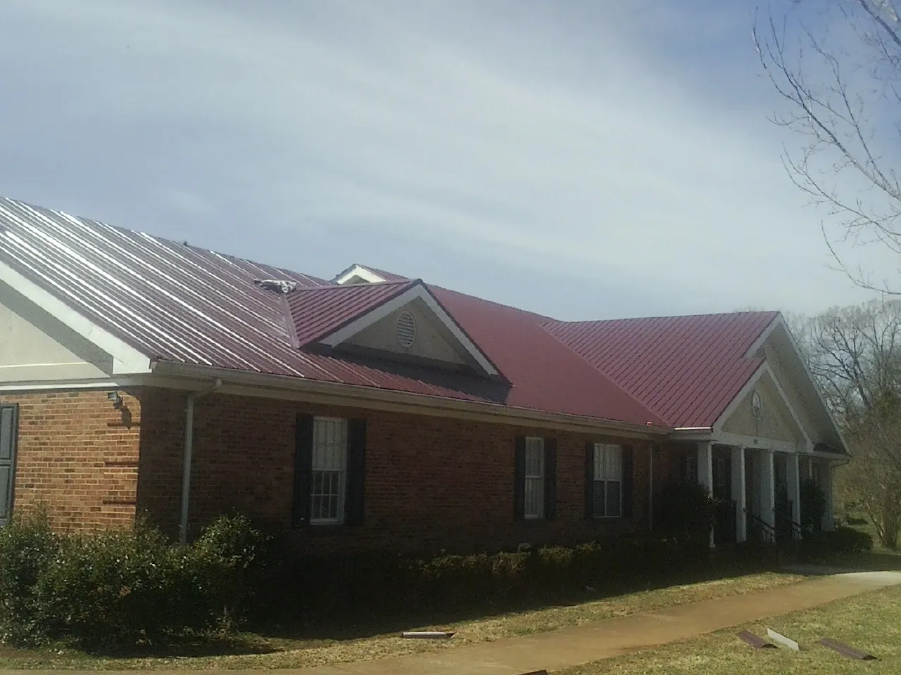 Red metal roof with gabled entries on a long brick building, from a Hail Damage Roof Repair job in Montpelier