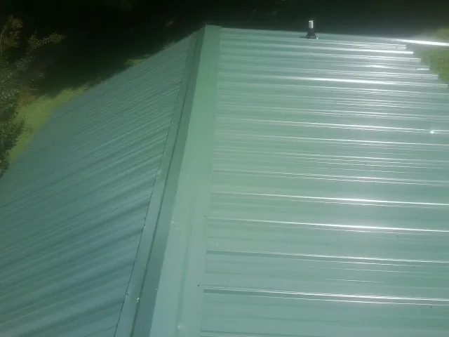 New green metal panels meeting at the ridge of a roof — Flat Roof Repair work by our crew in Montpelier