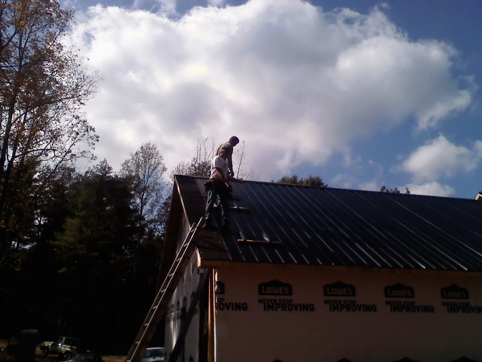 Roofer fastening dark metal panels high against a cloudy sky, from a Roof Inspection job in Montpelier